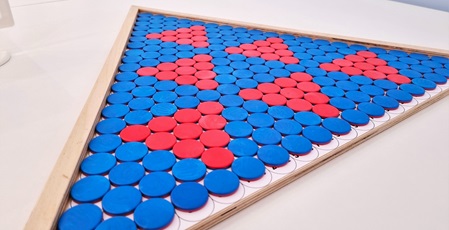 Runde blaue und rote Kunststoffplättchen in einem dreieckigen Holzrahmen