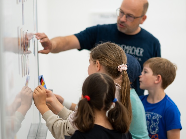 Mathemacher mit Kindern vor einem Whiteboard beim Lösen eines Exponats