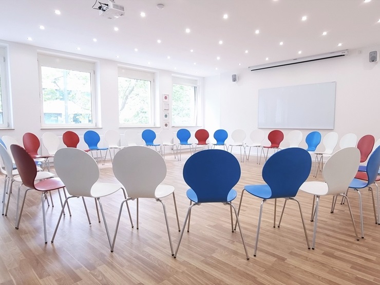 Stuhlkreis mit blauen, weißen und roten Stühlen in einem hellen Raum