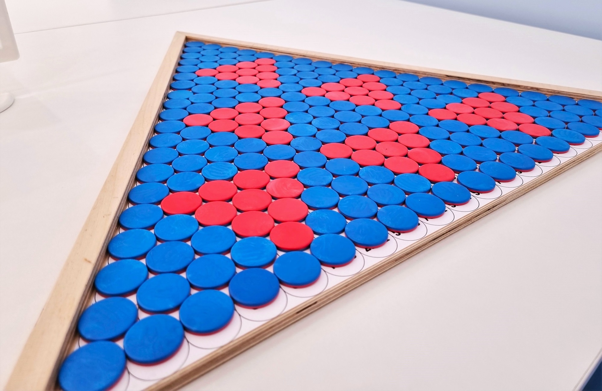 Runde blaue und rote Kunststoffplättchen in einem dreieckigen Holzrahmen